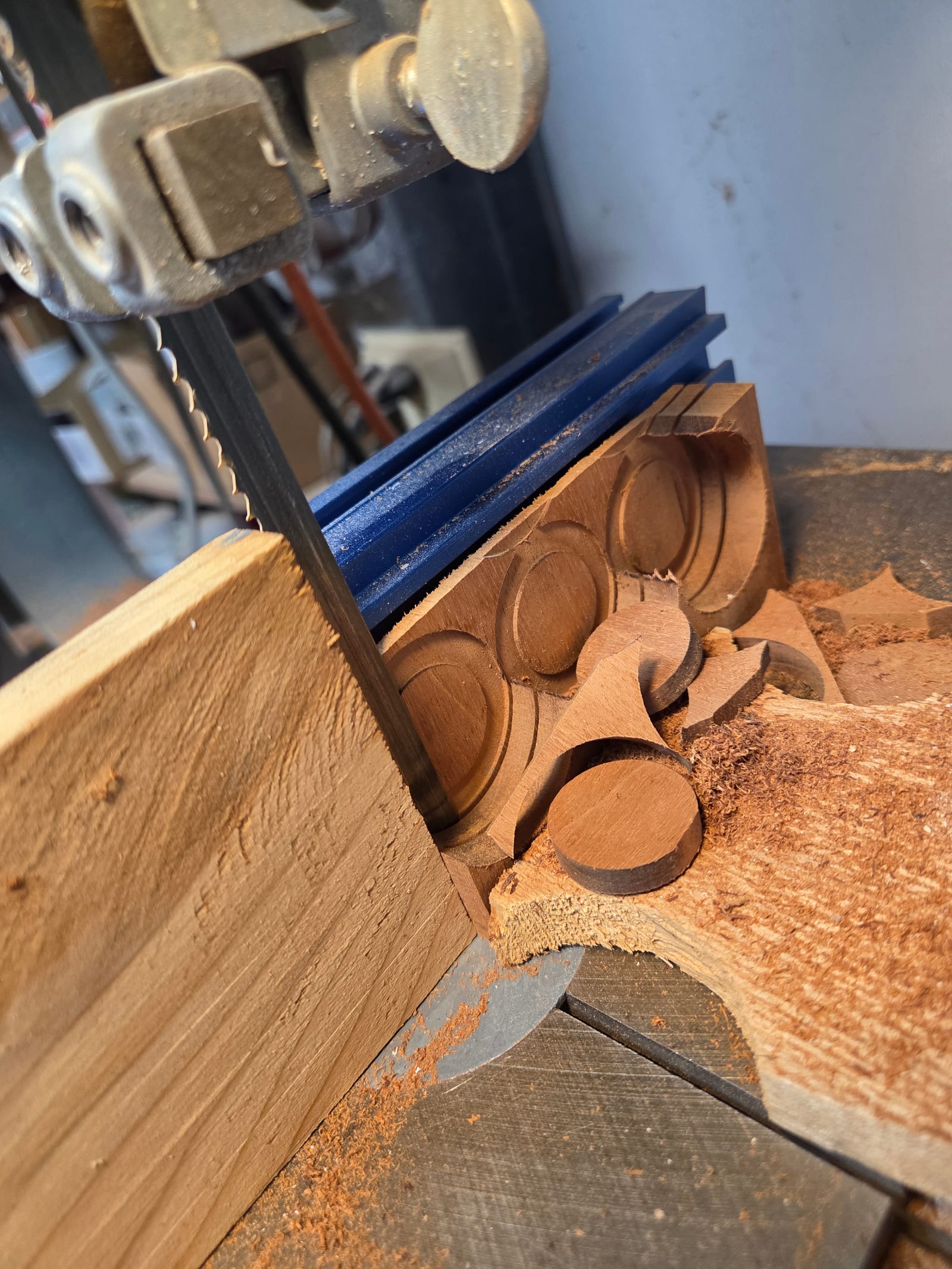 A bandsaw cutting round wood plugs from a strip of walnut, with finished plugs and sawdust on the table